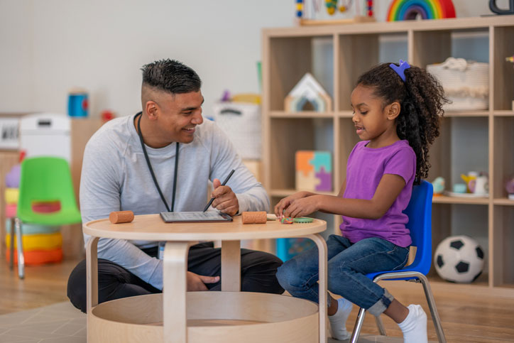 young man psychologist talking with little girl in counseling session